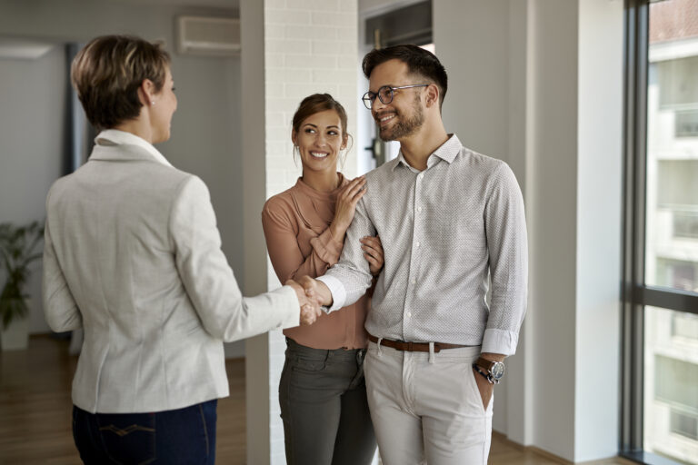 Young happy couple shaking hands with real estate agent
